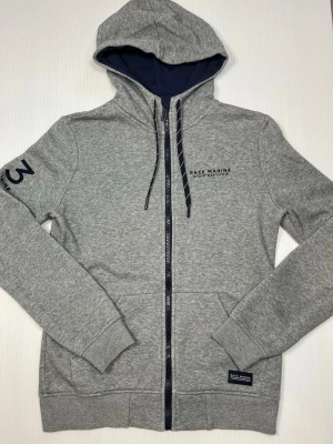 Race Marine ziphoodie – herr XS – gråmelerad – mycket bra skick - Säljer en Race Marine / Scandinavian Sportswear-ziphoodie i herrstorlek XS. Mycket bra skick. Färgen är gråmelerad med marinblå detaljer. Den har luva med dragsko, Race Marine-tryck på bröstet och siffran 83 tryckt på ärmen. En snygg och sportig hoodie som funkar till både träning och vardag.  • Skick: Mycket bra • Storlek: XS • Kön: Herr • Färg: Gråmelerad / marinblå detaljer • Märke: Race Marine / Scandinavian Sportswear