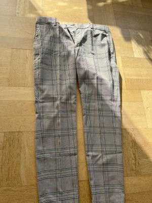 Rutiga kostymbyxor i beige och svart - Snygga kostymbyxor med klassiskt rutigt mönster i beige och svart. Byxorna har raka ben, bälteshällor och fickor både fram och bak. Perfekta för en stilren och trendig look. Materialet känns mjukt och följsamt.                         Slim fit från H&M