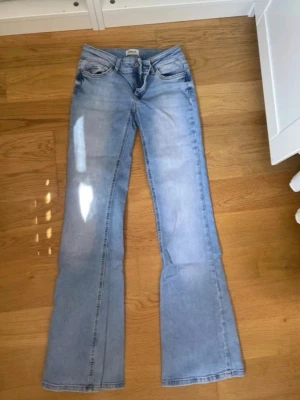 Ljusblå bootcut jeans - Säljer ett par ljusblå bootcut jeans med klassisk femficksdesign och normal midja. Jeansen har utsvängda ben och är tillverkade i denim med en snygg tvätt. Perfekta för dig som gillar retrostil och vill ha ett par bekväma jeans med cool passform.