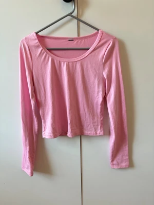 Ljusrosa långärmad topp - Säljer en enkel och stilren ljusrosa långärmad topp med rund halsringning. Toppen är croppad och har en mjuk, bekväm passform som passar perfekt till jeans eller kjol. Perfekt för dig som gillar en clean och söt look.