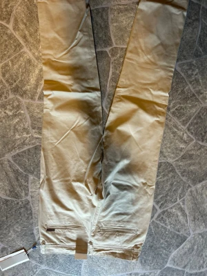 Beiga chinos i bomull - Snygga beiga chinos i rak modell med klassiska fickor bak och bälteshällor. Tillverkade i mjuk bomull som känns skön mot huden. Perfekta för en clean och stilren look.