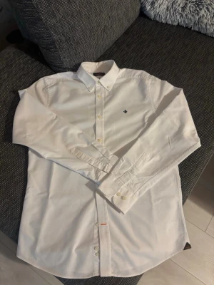Vit skjorta från Morris Stockholm - Klassisk vit skjorta från Morris Stockholm med button-down krage och diskret logga broderad på bröstet. Skjortan har långa ärmar, knappar framtill och är tillverkad i mjuk bomull. Perfekt för en clean och stilren look.