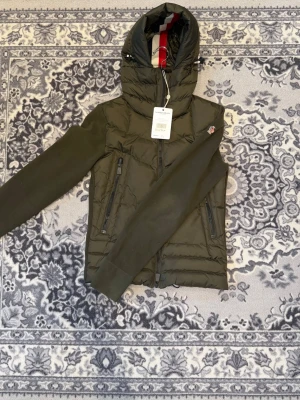 Moncler cardigan - Grön dunjacka från Moncler i stl S, normal i storleken. Har huva, dragkedja fram och två snedställda fickor med dragkedja. Köpt på vestiere för 490 eu Passade inte i storleken Verifiering från vestiere sitter kvar Bra skick.