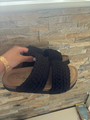 Svarta flätade sandaler från Duffy - Snygga svarta sandaler från Duffy med två breda, flätade band över foten. Sulan är beige och har en lätt upphöjd kant för extra komfort. Perfekta för sommarens alla outfits och ger en trendig touch till din stil.