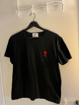 Svart t-shirt från Ami Paris - Snygg svart t-shirt från Ami Paris med det ikoniska röda hjärtat och bokstaven A broderat på bröstet. Klassisk passform och rund halsringning. Perfekt basplagg för en clean och stilren look.
