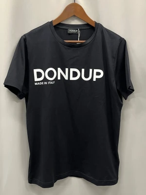 Svart t-shirt från Dondup - Svart t-shirt från Dondup med vit logga tryckt framtill. Klassisk rund halsringning och korta ärmar. Tillverkad i mjuk bomull för en skön och avslappnad look. Perfekt till jeans eller shorts för en clean och enkel stil.