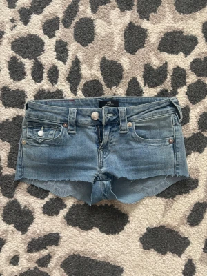Blå jeansshorts från True Religion - Säljer ett par blå jeansshorts från True Religion, har klippt bort trådarna då dom blev fula i tvätten. Dim ser så gott som nya ut. Är i storlek 24 men passar mig som har allt mellan 24-26 då dom är stretchiga.
