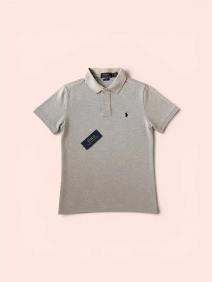 Beige pikétröja från Polo Ralph Lauren - Klassisk beige pikétröja från Polo Ralph Lauren med korta ärmar, krage och knappar framtill. Tröjan har den ikoniska broderade loggan på bröstet och är tillverkad i mjuk bomull. Perfekt för en stilren och avslappnad look.