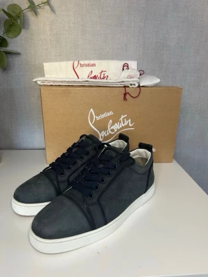 Blåa sneakers från Christian Louboutin - Stilrena blåa sneakers från Christian Louboutin med vita sulor och blåa skosnören. Skorna har en klassisk låg design och är tillverkade i mocka och läder. Perfekta för dig som vill ha en exklusiv touch på din outfit. Storlek 41 men passar 42 