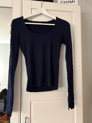 Mörkblå långärmad topp Gina Tricot - En enkel och stilren mörkblå långärmad topp från Gina Tricot. Toppen har rund halsringning och är figurnära i modellen. Perfekt att matcha med jeans eller kjol för en clean look.