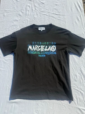 Maison Margiela svart t-shirt - Svart t-shirt från Maison Margiela med färgglatt tryck i blått, grönt och vitt framtill. Tveka inte att skriva vid frågor eller för fler bilder//Felkannn