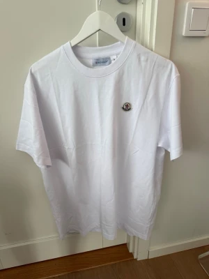 Vit Moncler t-shirt med logga - Snygg vit t-shirt från Moncler med klassisk rund hals och broderad logga på bröstet. Enkel och stilren design som passar till det mesta. Tillverkad i mjuk bomull för en skön känsla.