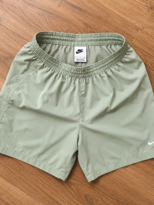 Ljusgröna shorts från Nike miller - Snygga ljusgröna shorts från Nike med elastisk midja och diskret vit logga på benet. Tillverkade i ett lätt och snabbtorkande syntetmaterial, perfekta för varma dagar eller träning.
