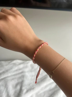 Färgglatt flätat vänskapsarmband - Säljer ett handgjort vänskapsarmband i flätad design med rosa, gult, orange och vitt garn. Armbandet har justerbar knut och avslutas med lösa trådar för en avslappnad look. Perfekt för dig som gillar färg och personliga accessoarer.💕