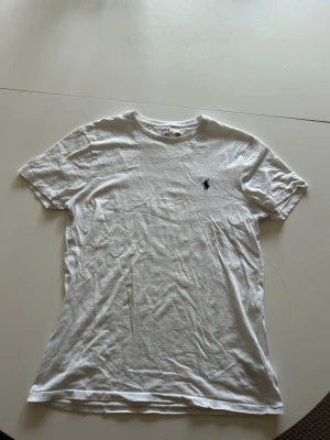 Vit t-shirt från Polo Ralph Lauren - Klassisk vit t-shirt från Polo Ralph Lauren med den ikoniska mörkblå broderade loggan på bröstet. T-shirten har rund halsringning och korta ärmar. Perfekt basplagg i mjuk bomull som funkar till allt.