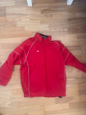New Balance Red Track Top - Den här varan kommer auktioneras ut på Sneakershyllan x Plick Live den Torsdagen 16 juli kl 19. Röd track top jacka från New Balance i storlek L. Slitage generellt och på trycket