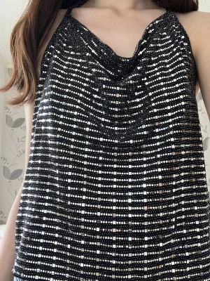 Glittrig svart halterneck topp - Säljer en glittrig svart halterneck topp med silverdetaljer. Toppen är ärmlös med tunna band som knyts i nacken 😊