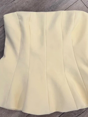 Ljusgul Zara topp - Trendig ljusgul korsettopp med axelbandslös design och markerade sömmar som ger en snygg siluett. Perfekt att styla med både jeans och kjol för en cool look. Säljer eftersom jag köpt en annan färg, den har en liten fläck på sig men jag tror de går bort i tvätten därav priset💕💕
