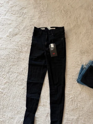 Levi's Mile High Super Skinny Jeans - Säljer ett par svarta Levi's Mile High Super Skinny jeans med hög midja och supertight passform. Jeansen är i stretchigt material. Helt nya & oanvända med etikett på. 