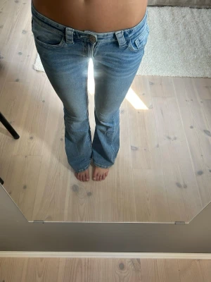 Blå bootcut jeans med låg midja - Säljer ett par ljusblå bootcut jeans med låg midja från Gina tricot. Jeansen har en snygg tvätt och är tillverkade i stretchigt denimtyg som sitter tajt över låren och släpper ut vid bensluten. Perfekta för en avslappnad och trendig look.