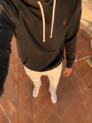 Ralph Lauren Hoodie – Svart - Exklusiv svart hoodie från Ralph Lauren med klassiska vita snören och den ikoniska röda Polo-loggan broderad på bröstet.  En stilren och mycket bekväm hoodie i en tidlös design som passar perfekt till både vardag och en mer exklusiv outfit. Hoodien är knappt använd och i mycket fint skick.