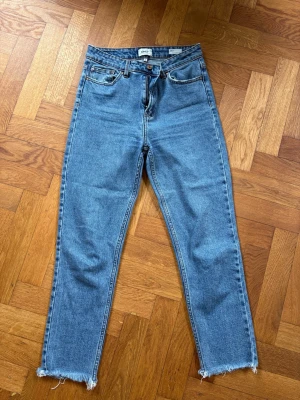 Blå high waist jeans från ONLY - Säljer ett par blå high waisted straight jeans från ONLY, modell EMILY. Jeansen har råa, fransiga benslut och klassisk femficksdesign. Perfekta för en avslappnad och trendig look. 