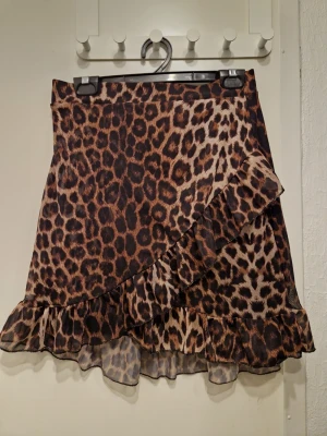 Leopardmönstrad volangkjol NLY Trend - Snygg kort kjol från NLY Trend med leopardmönster och volangdetaljer. Kjolen har omlottkänsla och är perfekt för dig som vill sticka ut med en trendig look. Materialet känns lätt och flowy.