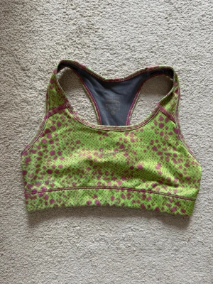 Grön sport-bh med rosa mönster Nike - Sport-bh från Nike i grön färg med rosa prickigt mönster. Brottarrygg och grå insida. Perfekt för träning och aktivitet. Nike-logga framtill som försvunnit något. Rökfritt hem. Kolla gärna mina andra annonser!