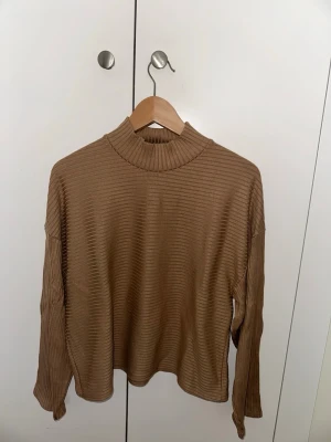 Beige ribbstickad tröja med polokrage - Snygg beige ribbstickad tröja med hög polokrage och långa ärmar. Tröjan har en avslappnad passform och är perfekt för lager-på-lager. Materialet är mjukt och stretchigt, vilket gör den bekväm att bära hela dagen.