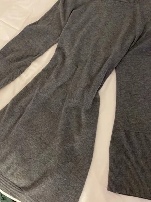 Grå stickad klänning från Adoore - Snygg grå stickad klänning från Adoore med rund halsringning och ribbade muddar vid ärmslut och hals. 