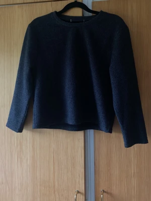 Mörkgrå enkel stickad tröja - En stilren mörkgrå croppad stickad tröja med rund halsringning och trekvartslånga ärmar. Tröjan har en rak passform och är gjord i ett mjukt, bekvämt material som passar perfekt till kalla dagar. Inga synliga detaljer eller mönster, vilket gör den lätt att matcha.