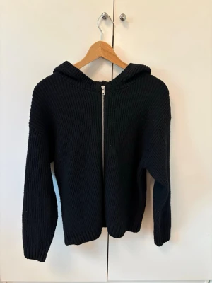 Svart stickad hoodie med dragkedja - Mysig svart stickad hoodie med dragkedja framtill. Tröjan har en luva och är ribbstickad för extra struktur. Perfekt för kyliga dagar och enkel att matcha med olika outfits. Har 2 till, en i vit och en grå, skriv till mig om ni har funderingar över dem också. 