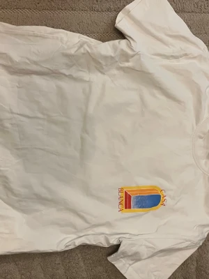 Casablanca t shirt - Vit t-shirt med färgglatt tryck från Casa Blanca. Framsidan har en liten logga och baksidan ett stort motiv i gult, blått och rött. Klassisk passform och rund halsringning. Perfekt för dig som gillar statement-plagg och snygga prints.