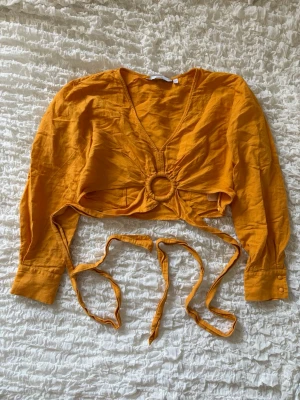 Jättefin topp från & other stories - Superfin och unik crop top i en härlig varmgul/orangefärg. Toppen har en jättesnygg ringdetalj framtill och långa band som kan viras runt midjan och knytas på flera olika sätt (se bilder för inspiration!). Perfekt till sommaren!!