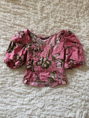 Blommig crop top med puffärmar - Säljer denna otroligt söta och somriga crop top från Zara i en jättefin rosa färg med grönt blommönster. Toppen har trendiga puffärmar, en smickrande fyrkantig urringning och smock/resår i ryggen vilket gör att den sitter superbra och är väldigt bekväm! Perfekta till sommaren☀️☀️💕💕