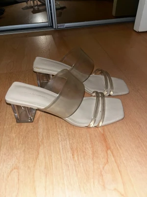 genomskinliga sandaler med transparent klack - Snygga sandaler med fyrkantig tå och breda, transparenta remmar i plast. Klacken är också transparent och blockformad, vilket ger en modern vibe. Sulan är beige och remmarna ger ett stilrent och trendigt intryck. Perfekta för att lyfta din outfit.