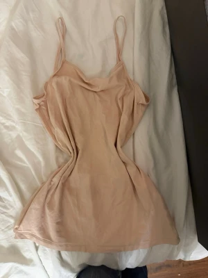 Beige linne med smala axelband - Säljer ett enkelt och stilrent beige linne med tunna axelband och mjuk, följsam passform. Perfekt för dig som gillar minimalistisk stil och vill ha något bekvämt. Materialet känns lätt och svalt mot huden.
