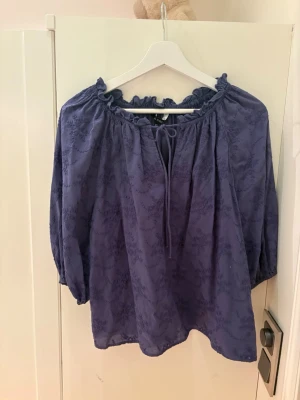 Lila blus med volangkrage XS - Supersöt lila blus från KappAhl i storlek XS. Blusen har volangkrage, knytning vid halsen och diskret blommönster i tyget. Lätt och luftig med trekvartsärm, perfekt för en chill och trendig look.
