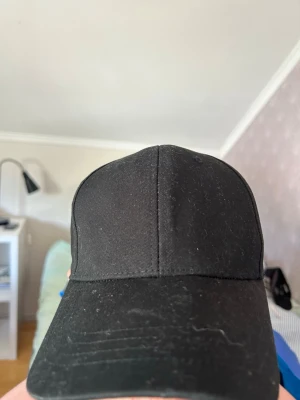 Svart klassisk keps med justerbar rem - En stilren svart keps i klassisk modell med böjd skärm och justerbar plastrem bak. Kepsen är tillverkad i ett slitstarkt tyg och passar perfekt för en avslappnad streetwear-look.
