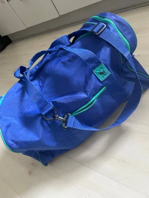 Blå duffelbag från WWF - Säljer en blå duffelbag från WWF med gröna detaljer och dragkedjor. Väskan har justerbar axelrem, bärhandtag och en praktisk ytterficka med dragkedja. Tillverkad i slitstarkt tyg och perfekt för gymmet eller resan.