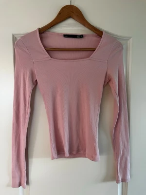 Ljusrosa ribbad långärmad topp lager 157 - Säljer en ljusrosa ribbad topp med lång ärm och fyrkantig ringning. Toppen är i stretchigt material och har en slim passform som sitter snyggt på kroppen. Perfekt att styla med jeans eller kjol för en trendig look.
