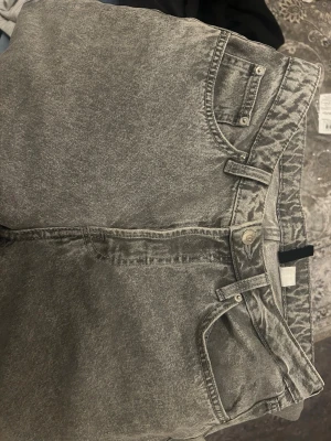 Grå tvättade raka jeans - Säljer ett par grå tvättade jeans med rak passform/baggy passform och klassisk femficksdesign. Jeansen har bälteshällor och knappgylf. Materialet är denim i bomull och färgen har en snygg tvättad look som ger en avslappnad vibe. 