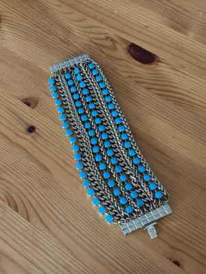 Snyggt guld armband med turkosa pärlor från Dubai - Snyggt brett armband i guldfärgad stainless metall med flera rader kedjor och turkosa pärlor. Armbandet är från Zerga i Dubai och är av mycket bra kvalitet. Det har ett coolt, chunky utseende och stängs med ett dekorativt spänne. Perfekt för dig som vill sticka ut med accessoarer.