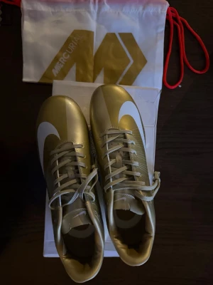 Nike Mercurial Vapor 16 Elite FG CR7 guld - Säljer ett par sällsynta Nike Mercurial CR7 i guldfärg. Skorna kommer med en exklusiv Nike Bowerman Prototype-låda, vilket gör dem extra intressanta för samlare och fotbollsentusiaster.  * Bra skick * FG-dobbar (naturgräs) * Original skosnören * Bowerman Prototype-box medföljer * Svårhittad modell  Perfekta för dig som samlar på äldre Mercurial-modeller eller vill ha ett unikt par CR7-skor.  📩 Skicka gärna meddelande vid frågor eller om du vill ha fler bilder. Öppen för seriösa bud.
