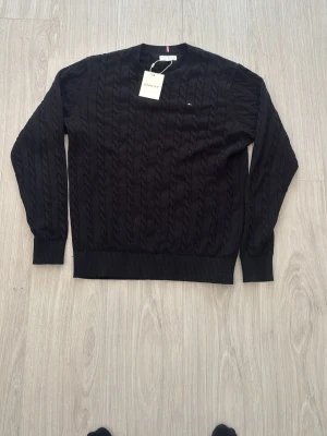 Tommy Hillfiger stickadtröja - Stilren svart kabelstickad tröja från Tommy Hillfiger som jag köpte för 1099kr från kidsbrandstore som är helt ny aldrig använd perfect för skolan med ett sjyst pris som även kan diskuteras 