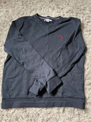Mörkblå sweatshirt från Polo ralph laruen - Klassisk mörkblå sweatshirt från polo ralph lauren med rund halsringning och diskret röd logga broderad på bröstet. Tröjan har ribbade muddar vid ärmslut och nederkant samt en enkel, stilren design som passar till det mesta.