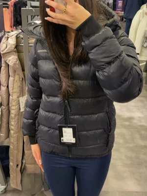 Svart dunjacka från Peak Performance - Snygg svart dunjacka från Peak Performance med huva och dragkedja framtill. Jackan har en puffig design, två sidofickor med dragkedja och diskret logga på bröstet. Perfekt för kalla vinterdagar och riktigt skön att bära. Köpt för ca 3000 kr för 3 år sedan.