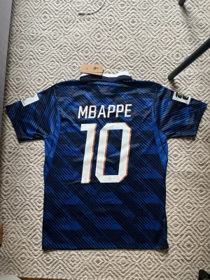 Frankrike fotbollströja Nike blå M - Säljer en blå Frankrike fotbollströja från Nike med nummer 10 Mbappe på bröstet. Tröjan har vita detaljer, vit krage och FFF-logga med två stjärnor. Tillverkad i Dri-FIT material som andas, perfekt för träning eller match.