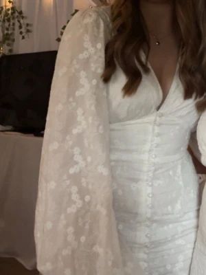 Vit broderad klänning med puffärm - Supersöt vit klänning med broderade blommor och stora puffärmar. Klänningen har v-ringning, knappar framtill och figurnära passform. Materialet ser ut att vara lätt och luftigt, perfekt för sommarens alla tillfällen. Använd 1 gång under ca 5 timmar 