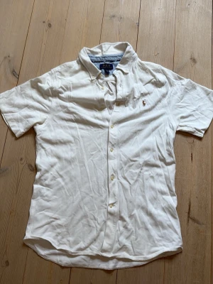 Kortärmad skjorta ralph lauren - En vit skjorta från ralph lauren. Storlek XL i barnstorlek men sitter som S i vuxenstorlek. Väldigt litet hål vänster bak som ses på bild 4. Ostruken :), sorry. 